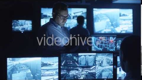 Security Officer Using Tablet in a Dark Monitoring Room Filled with Display | VideoHive 14742465