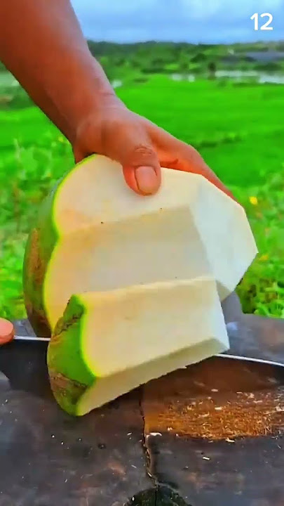 Mango peeled fresh—white flesh gleams against green field and morning sky