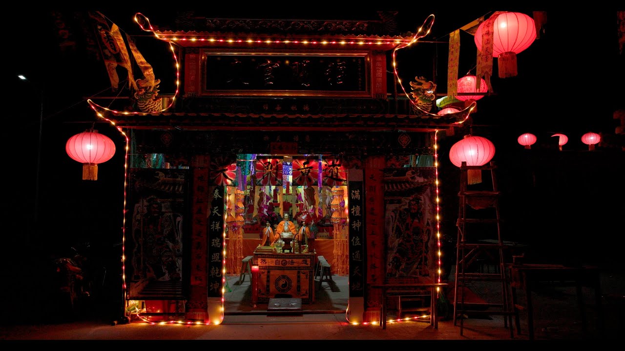 Color still from Da Jiao (dir. Boya Lei, 2025).  Brightly illuminated temple entrance decorated with red lanterns and colorful banners. 