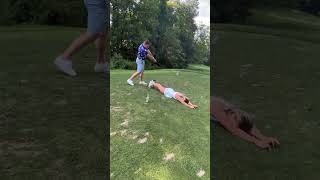 Guy hits golf ball sitting on tee between girls rear with club