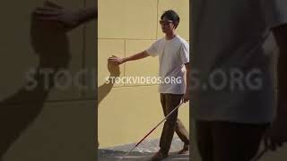 blind Asian man walking along a wall with cane