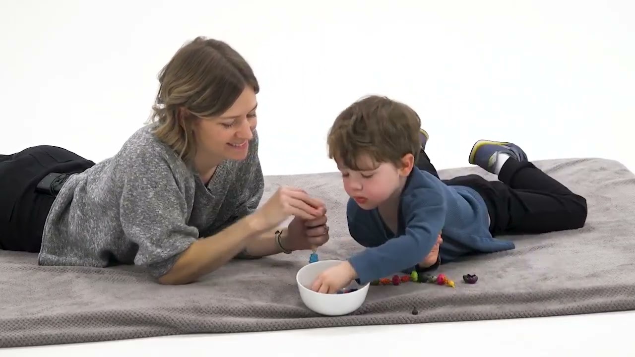 A woman and boy use Medbridge resources to play with items on a blanket.