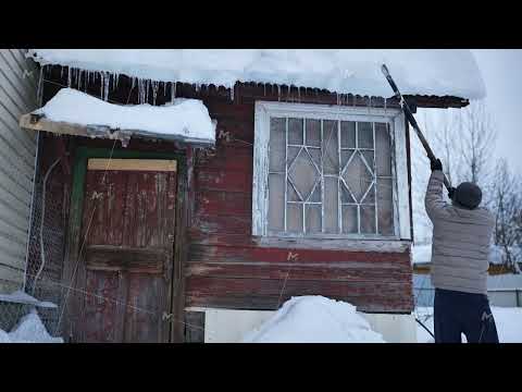 Man removing dangerous icicles and snow from rustic wooden house roof in winter