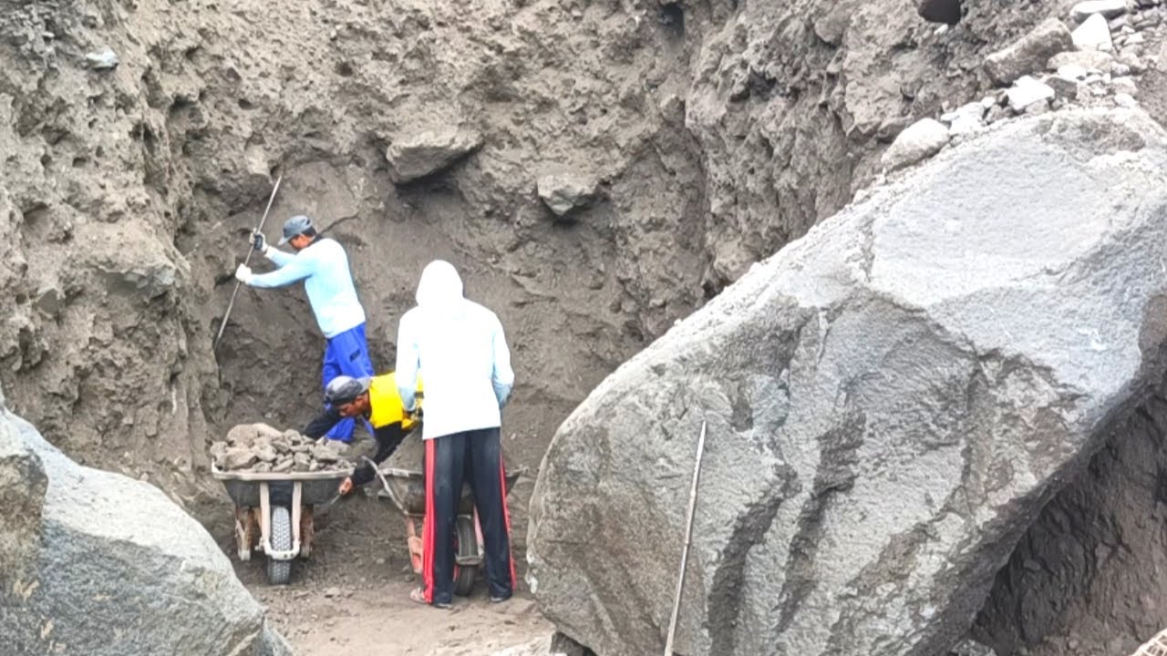 As three sand miners search and sift through black sand between two ...