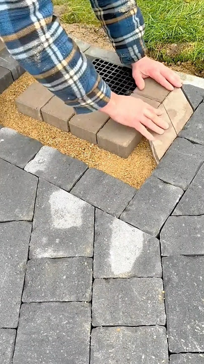 Worker installing paving stones around drainage grate