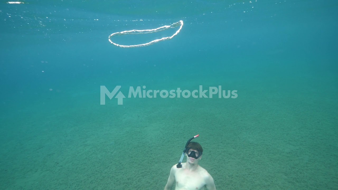A male free diver underwater and a bubble ring ascending in slow motion.