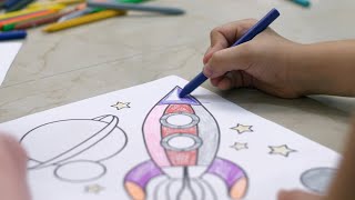 Kids coloring on a sheet of paper with crayons while sitting on the floor