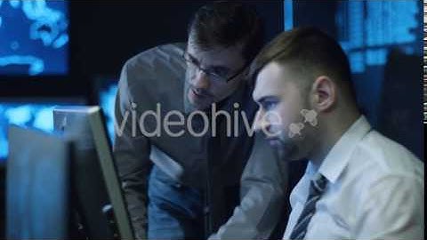 Two IT Programmers are Working on Computer in Dark Office Room Filled with Display Screens | Stock