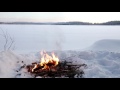 A campfire is burning bright at a snow-covered frozen lake- a relaxing winter video