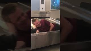 Guy rides on baggage claim conveyor belt while grandma trips over luggage