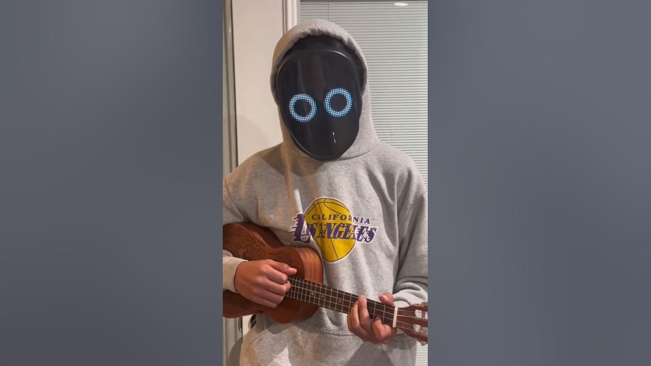 A boy wearing a face mask plays ukulele in front of a laptop Stock