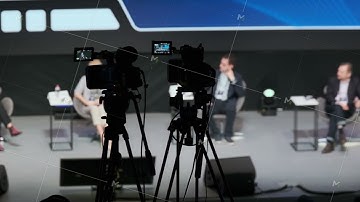 Panel discussion on stage with cameras filming as experts speak