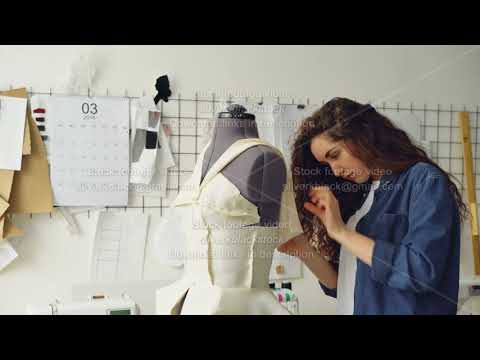 Young pretty seamstress is busy adjusting clothing on tailoring dummy with sewing pins. Women's