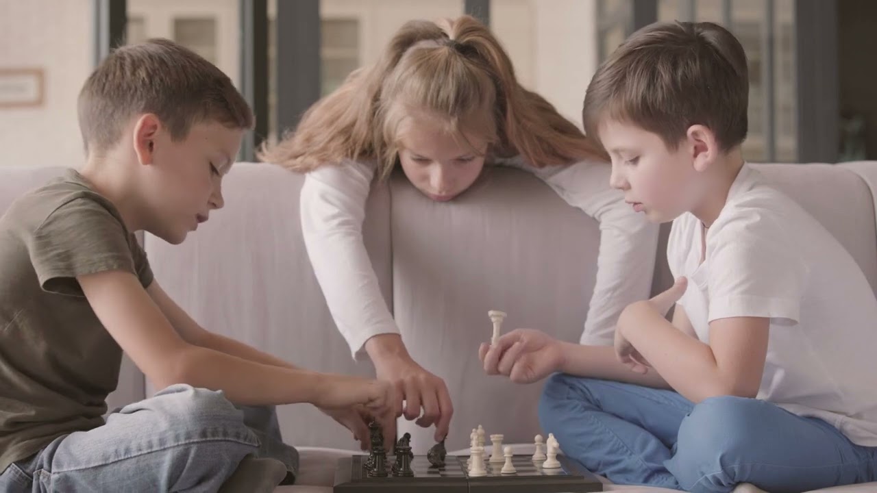Two boys and a girl, sitting on a sofa, playing with chess pieces, on a boring afternoon.