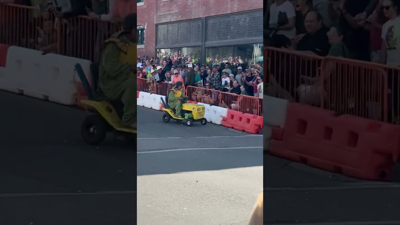 Boy rides downhill in soapbox derby then crashes into boy in yellow shirt in the audience