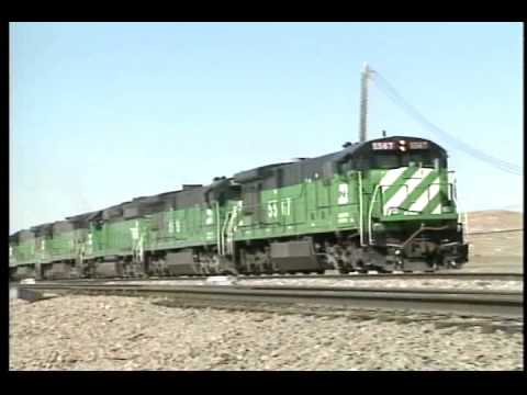 The amount of coal transported by rail each year continues to grow. The Burlington Northern and the Chicago & North Western benefit greatly by hauling this coal out of the Powder River Basin of Wyoming. Watch as each railroad uses its own main line, and then work together on the joint line moving the coal out of the state. The Burlington Northern's 5th Sub from east of Gillette, southeast through Newcastle is the easternmost line. This section of railroad hosts much of the BN's coal traffic and also has plenty of general freight and priority trains as well. The Chicago and North Western operates over a section of its old "Cowboy Line" from Crandall to Shawnee toward the mines. On the Powder River Sub, the C&NW's Dash 9-44 and AC4400CW locomotives lead trains along with a sampling of Union Pacific power. Then the two railroads join together on the BN's 10th Sub, which is also the BN/CNW joint line. This corridor is the direct link to a majority of the Powder River Basin coal mines. Copyright 1995, C. Vision Productions Color/80 Minutes