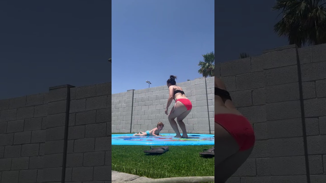 Woman in bikini records her and her son playing on water mat then boy slips and hits back of head