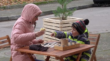 Woman with kid playing checkers and sharing snack in cold cafe