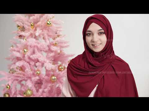 Portrait of muslim woman in hijab looking at camera and smiling standing against Christmas tree