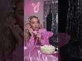 Stylish girl in pink tracksuit talks on a retro phone, lying on a shiny pink bed with popcorn .