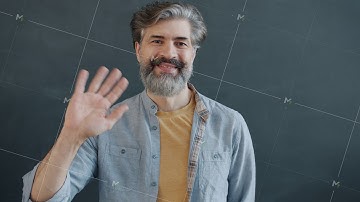 Portrait of friendly mature man waving hand looking at camera and smiling on gray background