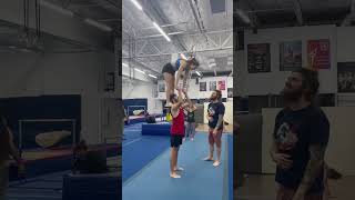 Woman doing gymnastics gets lifted over guy in red shirt while holding his hand then falls on mat