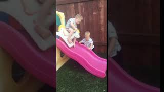 Boy goes down slide with toy rocking horse then falls off and lands on his little brother