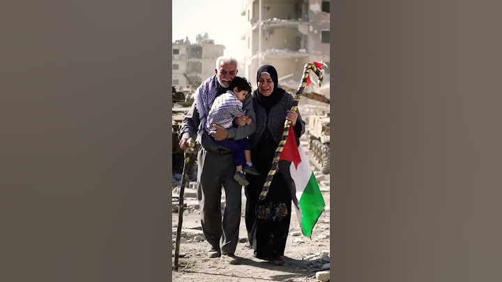 Seorang kakek dan nenek dari palestina menggendong cucunya melewati gedung yang hancur