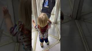 Little boy with blonde hair walks into glass maze house and bumps head