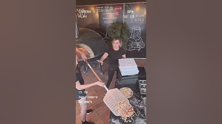 Two pizza restaurant employees have trouble picking up the pizza and getting it into the o