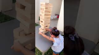 Girl playing Jenga pulls out block then all pieces fall on her head
