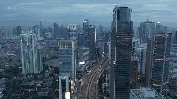 Aerial rising dolly shot following busy multi lane traffic between modern skyscrapers in the dusk in