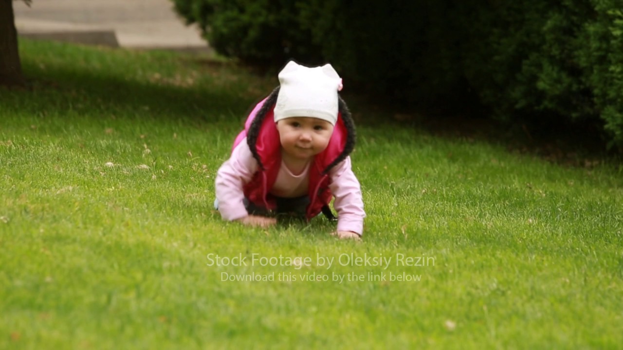 Cute little baby-girl is crawling in the green fall-meadow in the city ...