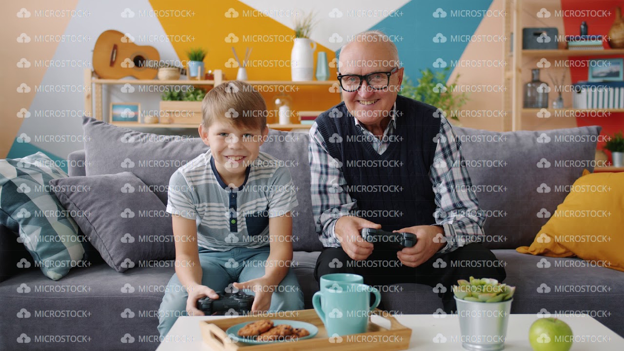 Grandfather and grandson are playing video game sitting on sofa at home