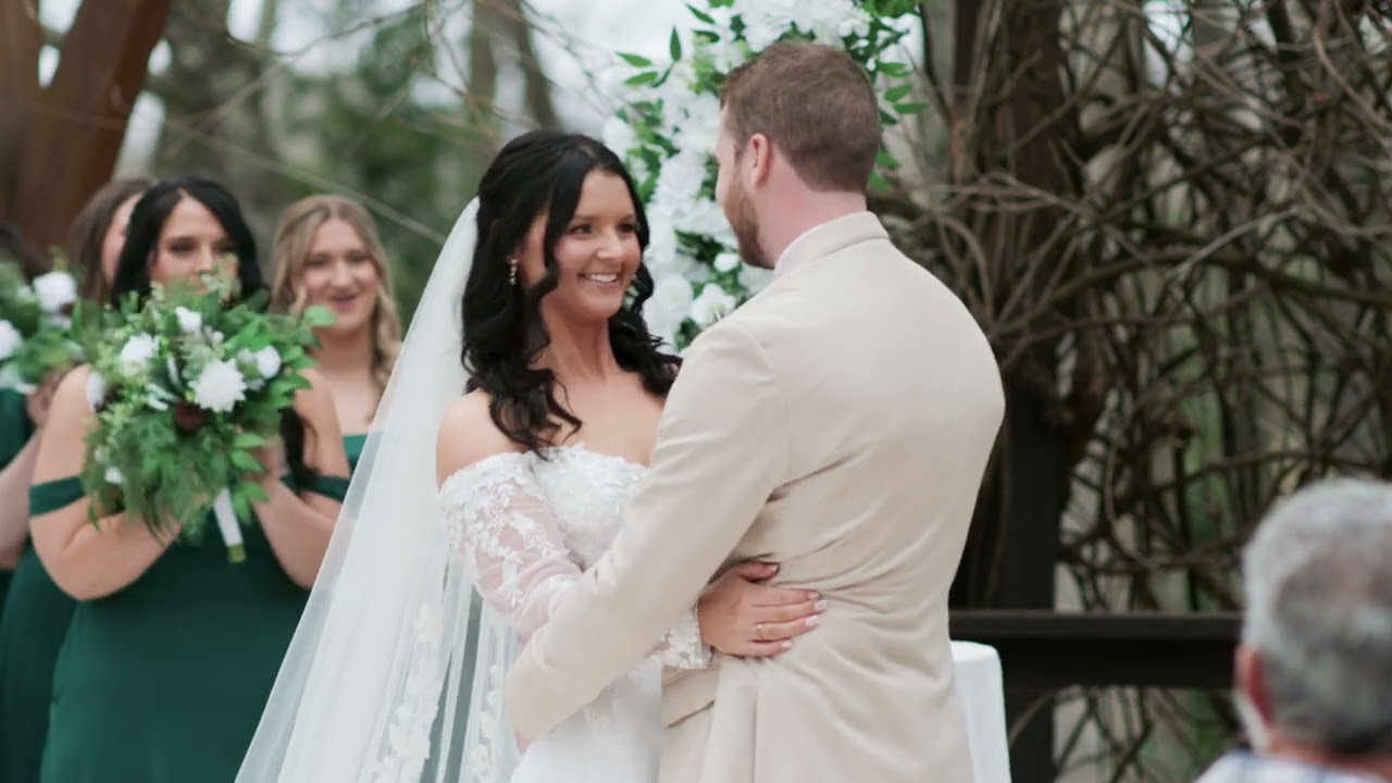 Groom in a tan suit hugging his bride as bridesmaids with green bouquets smile at The Garden Cottage in Dahlonega, GA