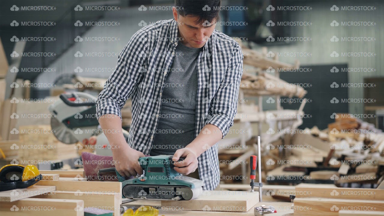 Young man working in wood workshop using polishing machine to polish wood