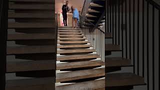 Guy attempts to slide down headrail while holding beer can then falls down stairs