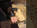 A person is carving and smoothing a wooden board using a hand chisel