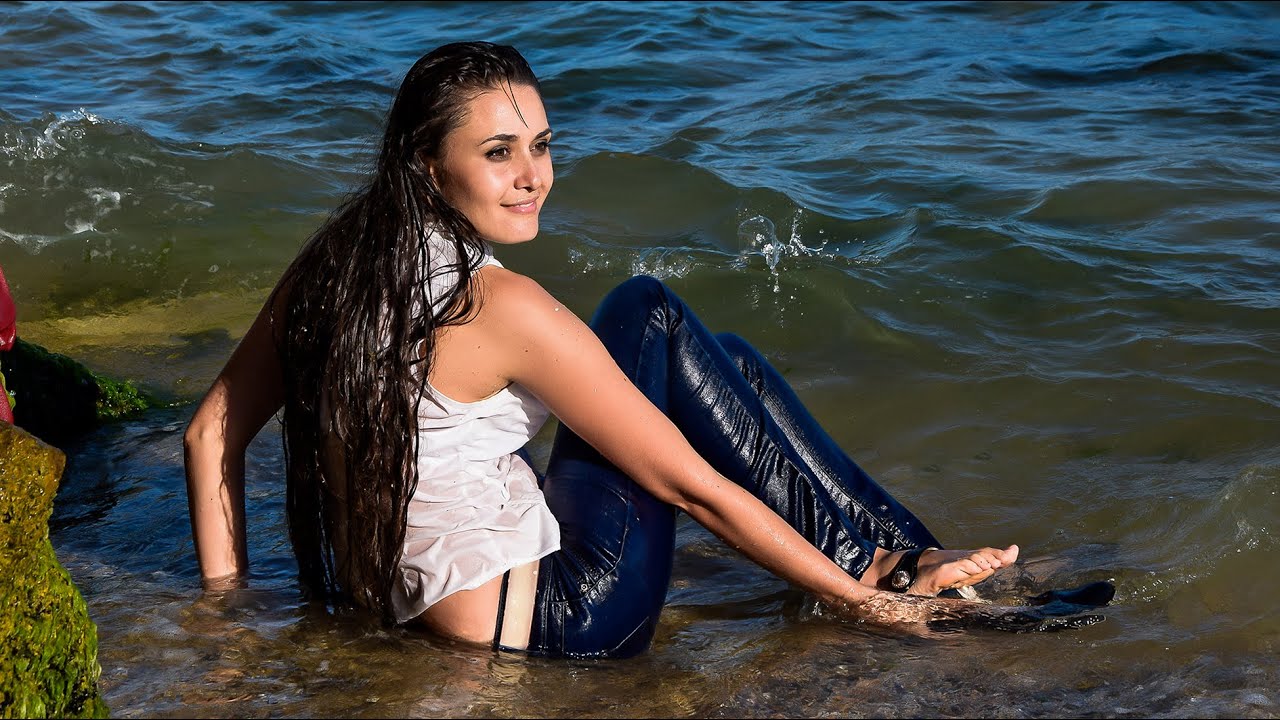 GIRL WITH A BEAUTIFUL FIGURE POSE BRIGHTLY ON THE BEACH BY THE SEA IN WET CLOTHES FOR WETLOOK VIDEO