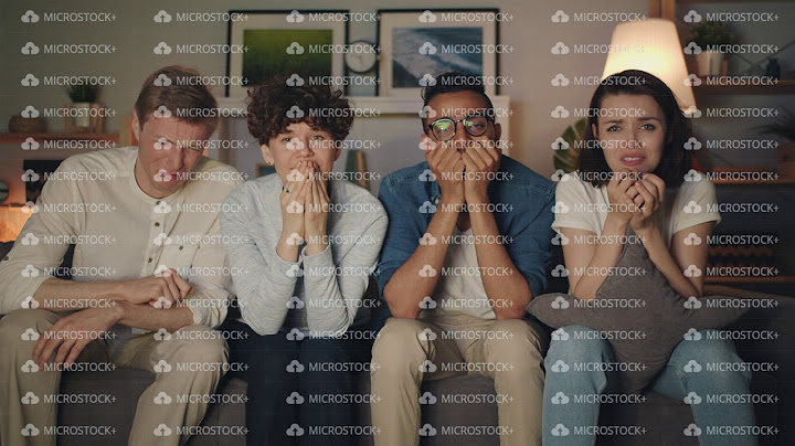 Sad young people watching TV at night crying wiping faces with paper tissues