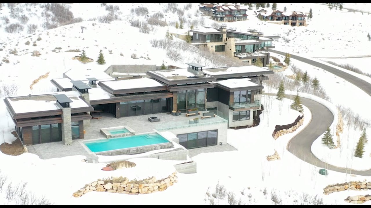 Aerial view of a modern luxury home with a swimming pool, surrounded by snow-covered landscape and mountain scenery, showcasing real estate potential for marketing.