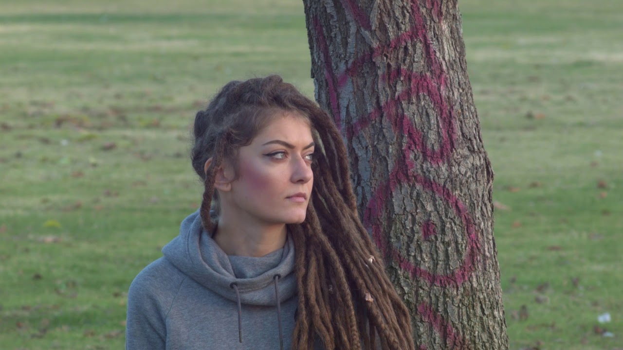 Full of hope young white rasta girl with dreadlock sitting in a cold public park alone and happy