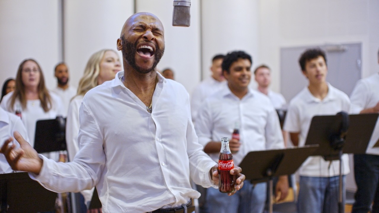 Man singing with a group while holding a glass bottle of Coca-Cola