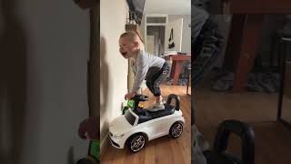 Boy stand and balances on steering wheel of toy car then pushes himself off wall
