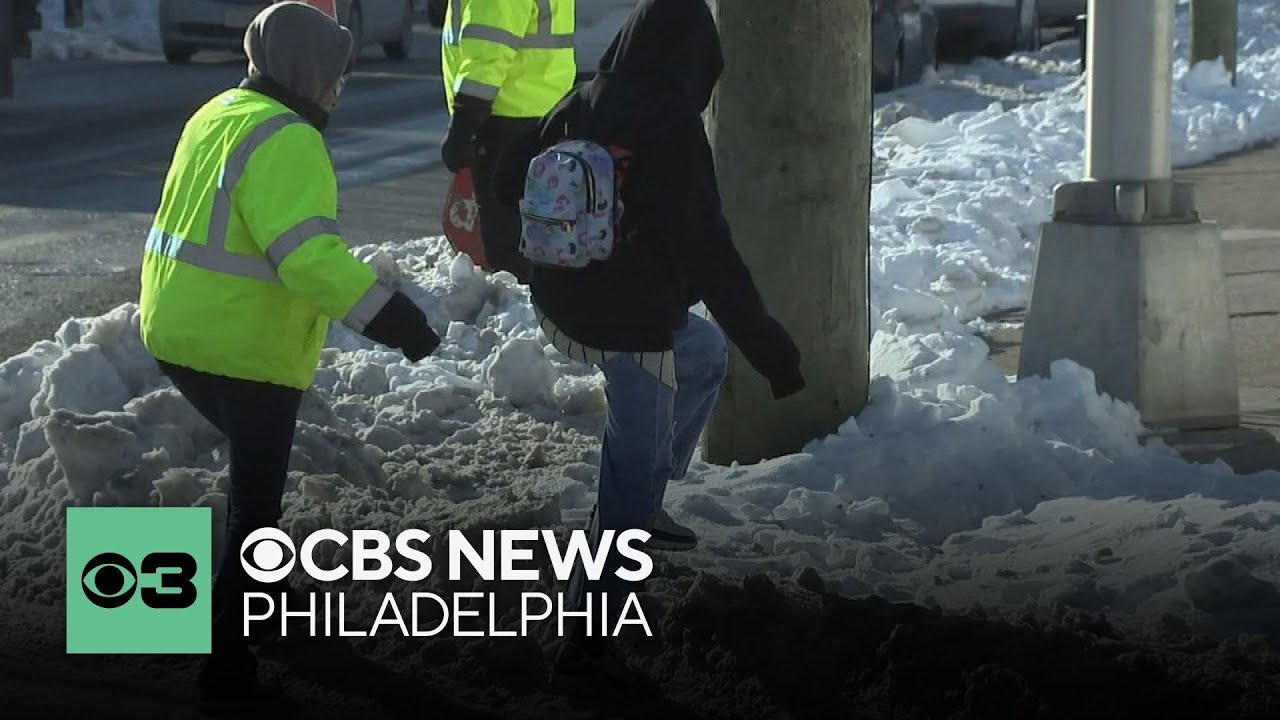 Gloucester City, New Jersey, crossing guards help students cross piles of snow at busy intersection