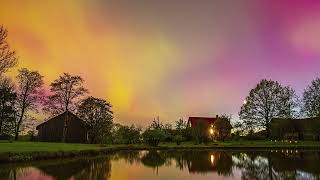 Brilliant aurora borealis over a farm with the sky colors reflecting off the lake   time lapse