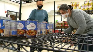 two women in masks looking for canned food on shelves