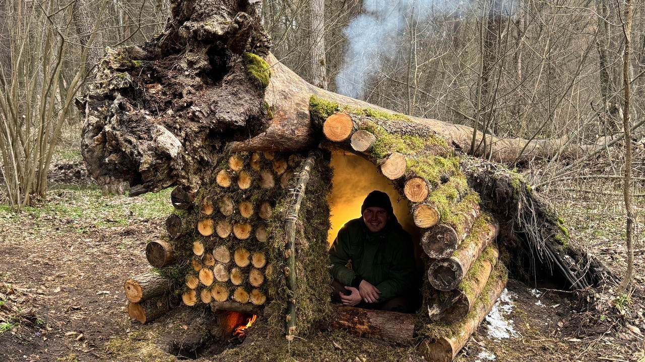 Building a log shelter from the Snow under the trunk of a hanging tree. A warm bed. Catch and cook