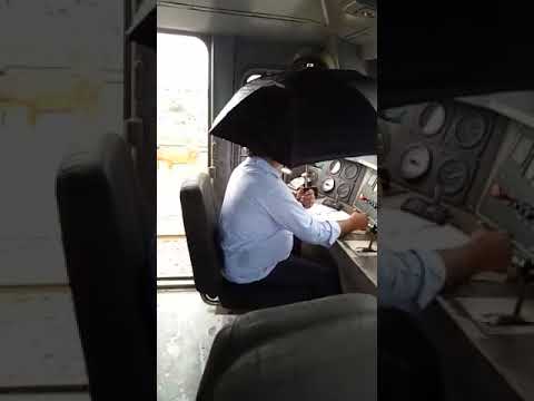 Train driver holds umbrella in dripping cabin