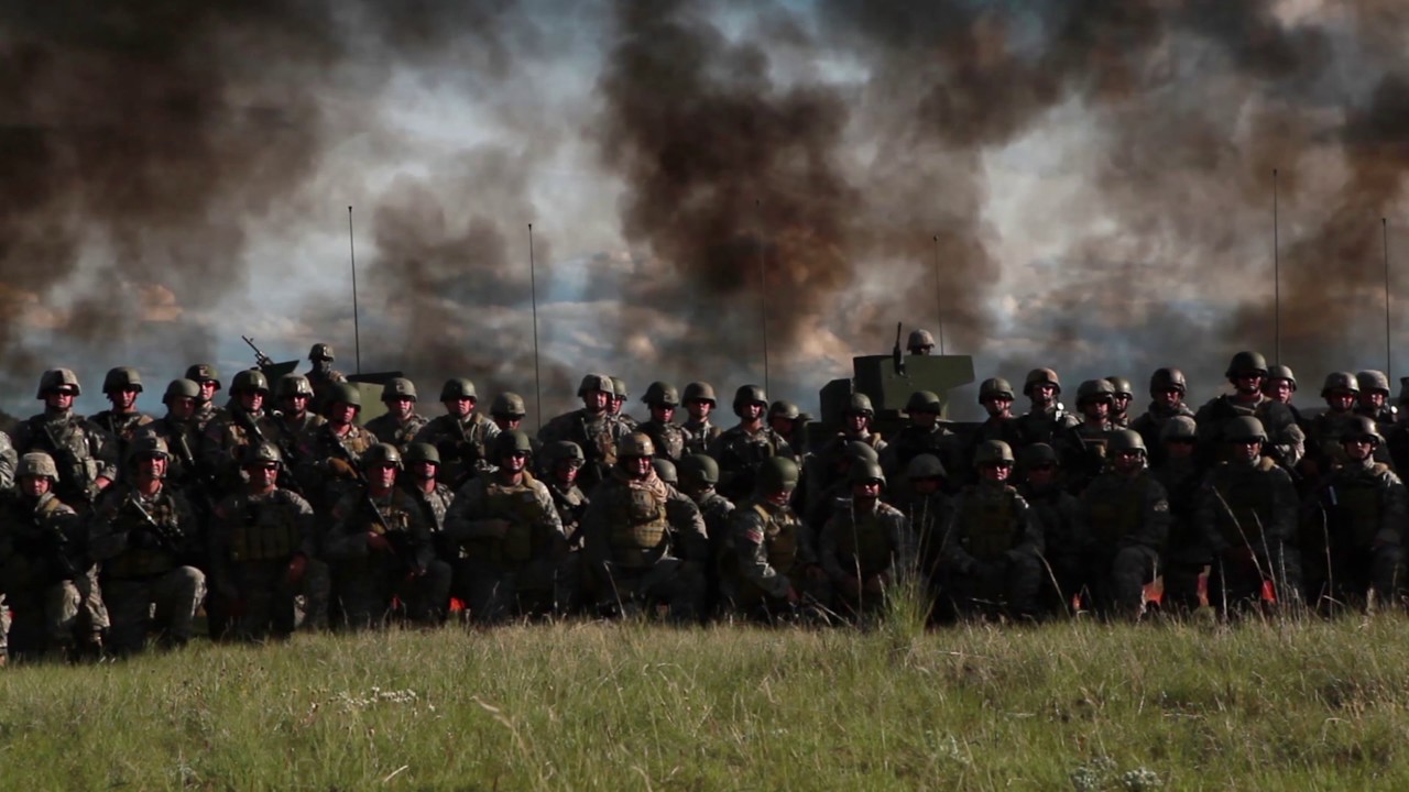 Panning shot of a group of soldiers lined up with explosion behind